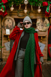 a lady in a black top, a red overcoat, a pair of grey pants and a green scarf
